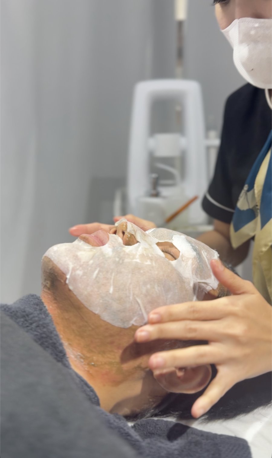 A therapist placing a calming sheet mask on a client's face